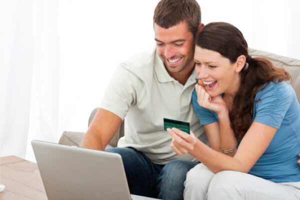 Happy couple looking at their accounts online sitting on the sofa at home